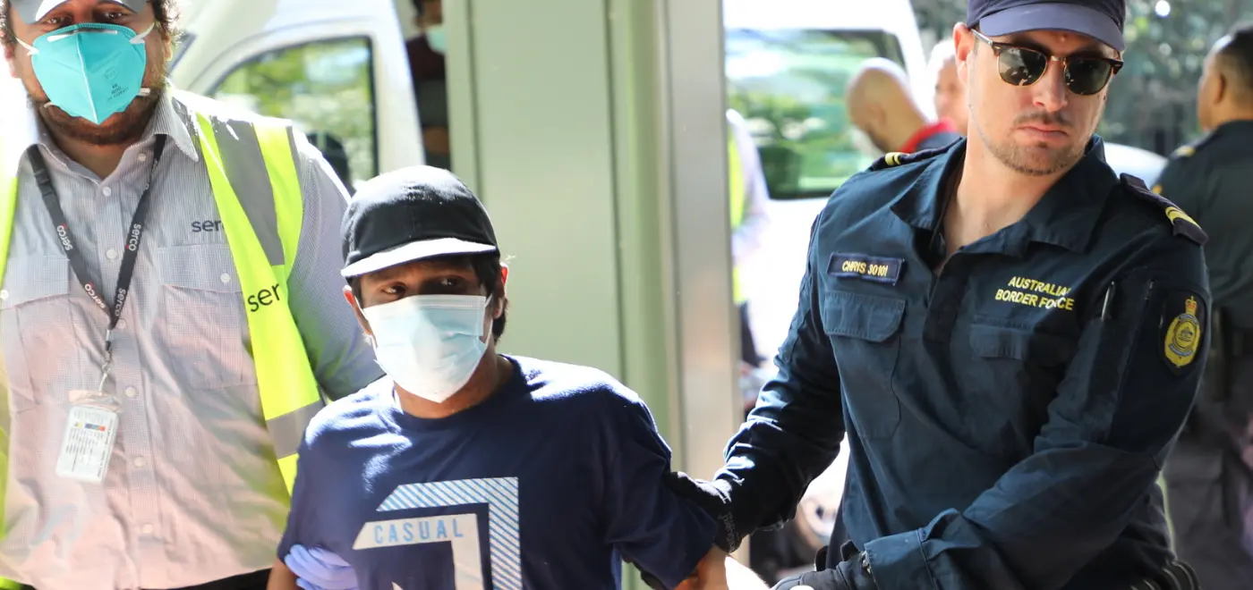Australian Border Force officer escorting a detained fisherman wearing a mask and casual clothing