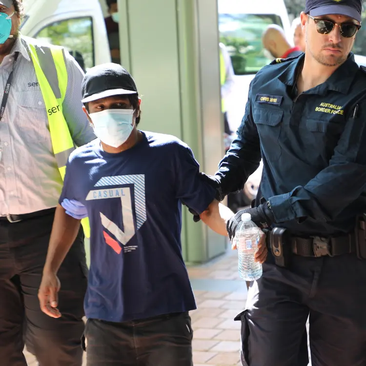 Australian Border Force officer escorting a detained fisherman wearing a mask and casual clothing