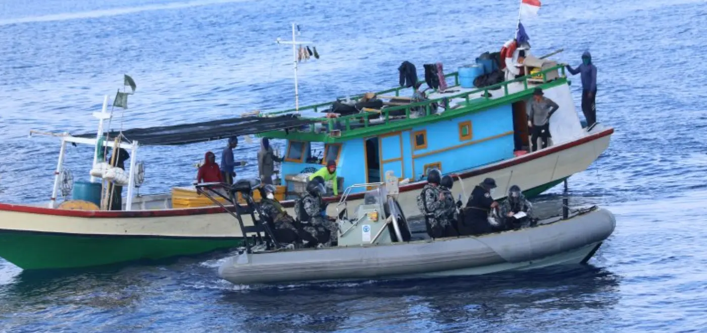 Petugas maritim di perahu karet bermotor naik ke kapal ikan ilegal dengan beberapa nelayan di atasnya